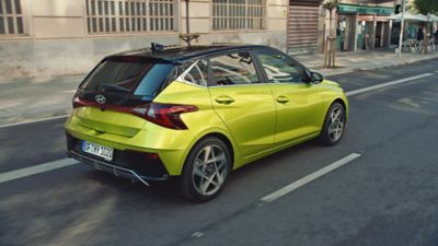 Ein grüner Hyundai i20 fährt von hinten gesehen eine Straße entlang.